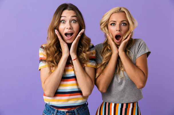 Two pretty shocked young girls friends standing isolated over violet background, screaming - Foto, Bild