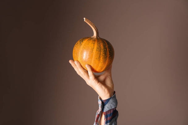 Female hand with whole fresh pumpkin on color background - 写真・画像