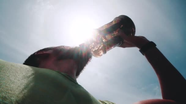 Bottom view of athlete drinking water from bottle after intense exercise. Thirsty man having cold refreshment during hot day - video in slow motion - Materiaali, video