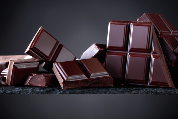 Broken chocolate pieces on a black background. Copy space for your text. - Photo, Image
