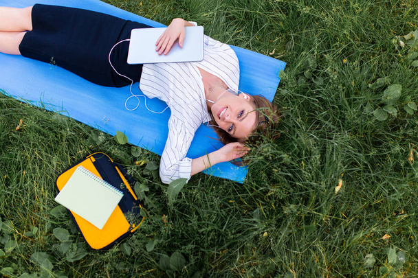 Woman resting in the park lying on the grass with a laptop and listening to music - Valokuva, kuva