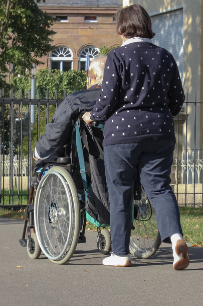 Κυρία με ανώτερος άνθρωπος στην αναπηρική καρέκλα στο πάρκο της πόλης, σε πτώση το βράδυ, στη νότια Γερμανία - Φωτογραφία, εικόνα