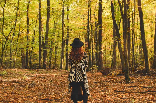 Girl of redheads in knitted ethnic ponchos, trousers and a backpack. The warming of the atmosphere is warm and the sun.Portret in the forest. Natural background. Woman travels Travel  photo - Photo, Image