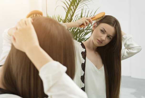 Отражение в зеркале молодой женщины, расчесывающей длинные волосы
  - Фото, изображение