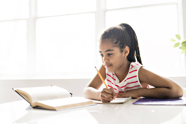 A cute Black girl doing homework at home - Foto, Imagem