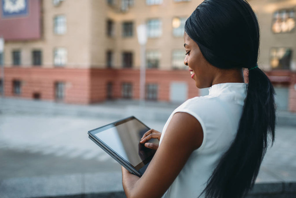Geschäftsfrau blickt auf Laptop-Bildschirm vor Bürogebäude. Lächelnde schwarze Geschäftsfrau in weißer Bluse arbeitet draußen am PC - Foto, Bild