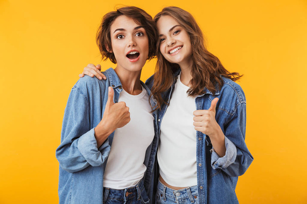 Photo of cute young women friends posing isolated over yellow background showing thumbs up. - Фото, зображення