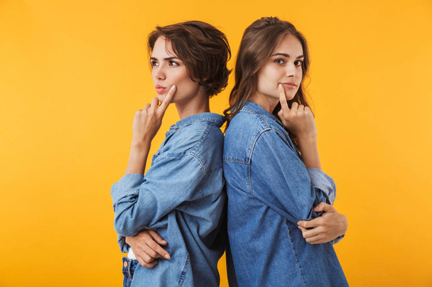 Image of serious thoughtful young women friends isolated over yellow wall background. - Fotoğraf, Görsel