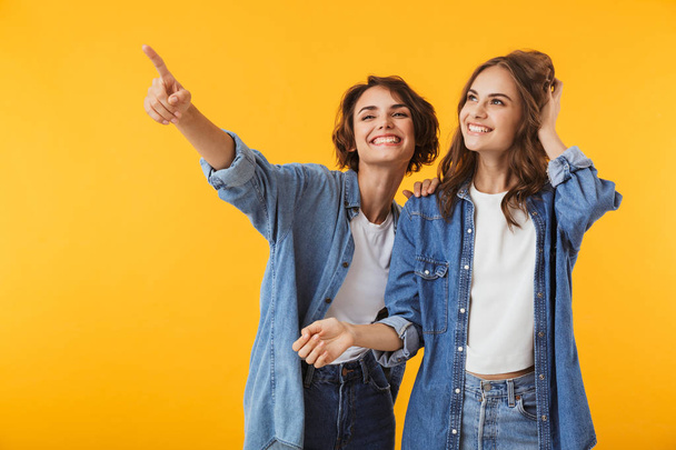 Image of amazing smiling emotional young women friends posing isolated over yellow background pointing. - Фото, изображение