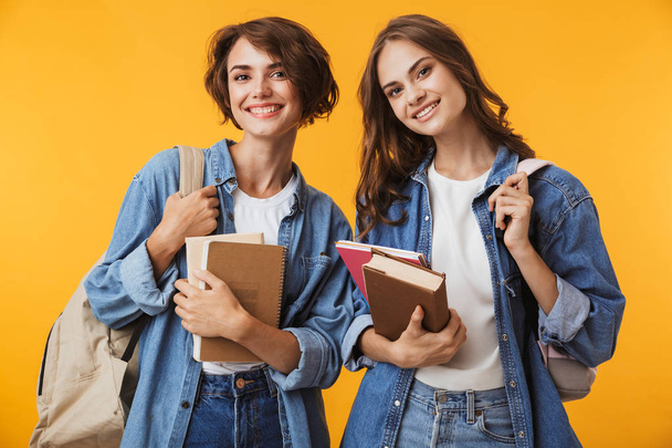 Photo of cheerful happy emotional young women friends posing isolated over yellow background holding books. - Valokuva, kuva