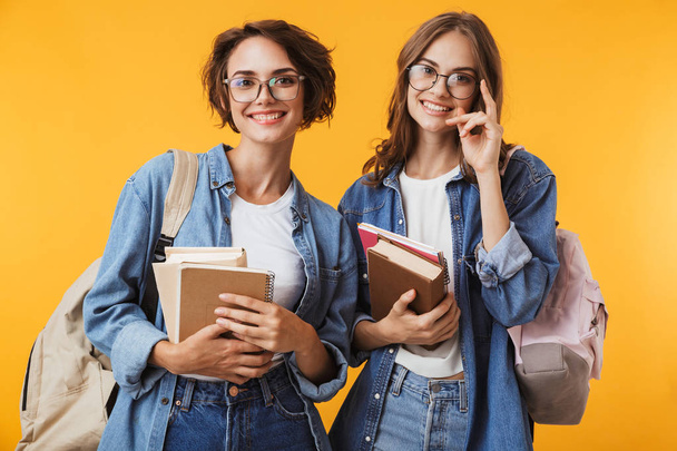 Photo of cheerful happy emotional young women friends posing isolated over yellow background holding books. - Photo, Image