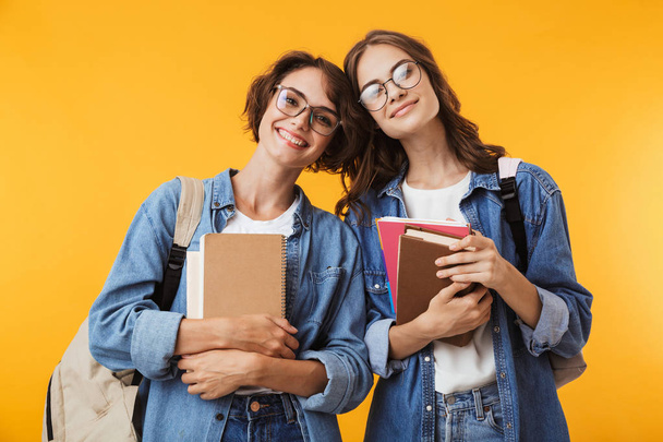 Image of cheerful happy women friends isolated over yellow wall background holding books. - Photo, Image