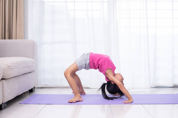 Asian Chinese little girl practicing yoga pose on a mat in the living room at home - Foto, immagini