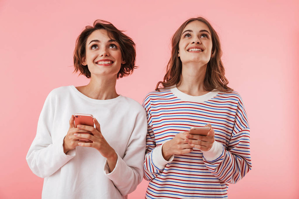 Image of happy women friends isolated over pink wall background using mobile phones. - Photo, image