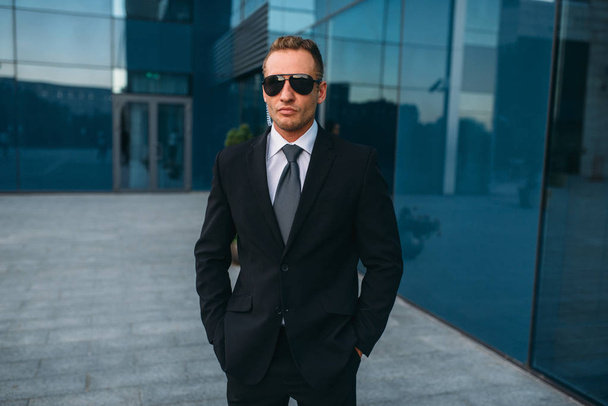 Male bodyguard in suit and sunglasses outdoors. Guarding is a risky profession. Professional guard, politician persons and businesspeople safeguard, safe control - Photo, Image