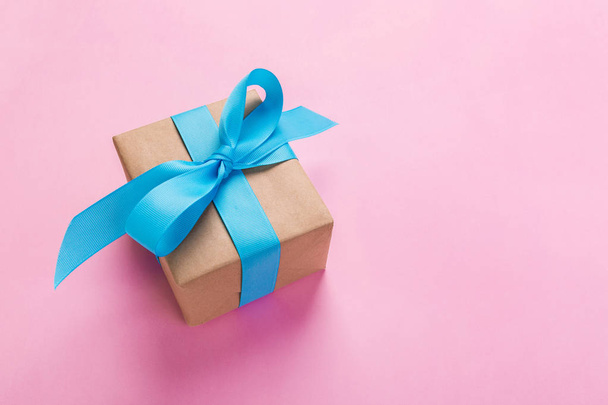Geschenk verpackt und dekoriert mit blauer Schleife auf rosa Hintergrund mit Kopierraum. flache Lage, Draufsicht. - Foto, Bild