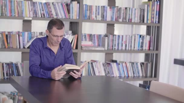 Σοβαρός άνθρωπος ανάγνωσης βιβλίου σε μια βιβλιοθήκη - Πλάνα, βίντεο