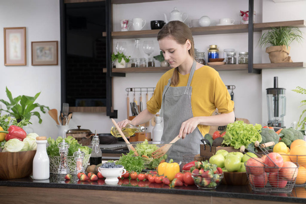 Healthy young woman in a kitchen preparing fruits and vegetables for healthy meal and salad - Foto, Imagen