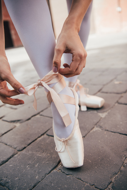 close-up partial view of young ballerina tying pointe shoe on street - Foto, Imagen