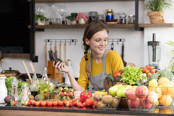 Terve nuori nainen keittiössä valmistamassa hedelmiä ja vihanneksia terveelliseen ateriaan ja salaattiin
 - Valokuva, kuva