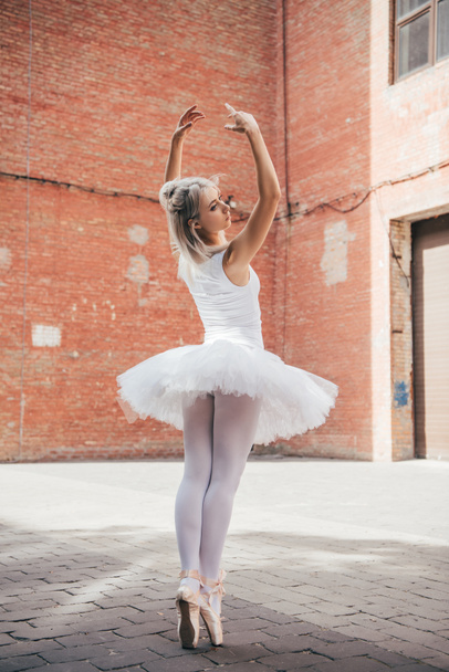 back view of young ballerina in tutu and ballet shoes dancing on street - Foto, imagen
