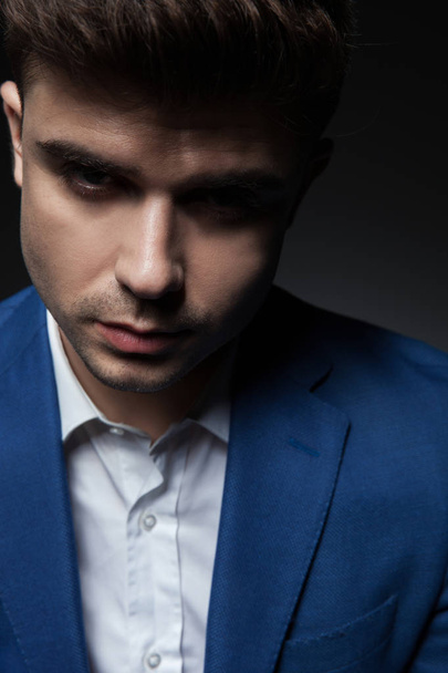 close up of sexy smart casual man in blue suit looking seductively while standing on dark grey background - Photo, Image