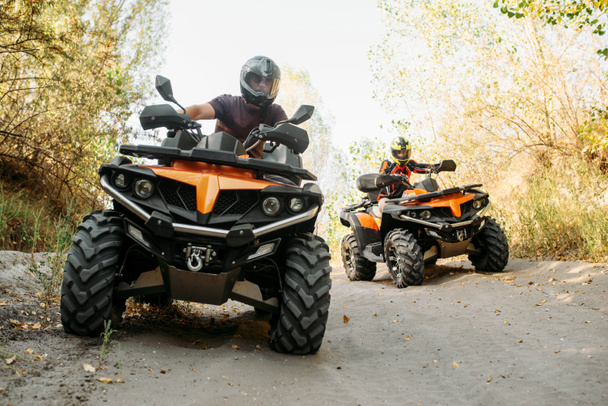 Two quad bike riders in helmets travels in forest, front view. Riding on atv, extreme sport and travelling, quadbike adventure - Photo, Image