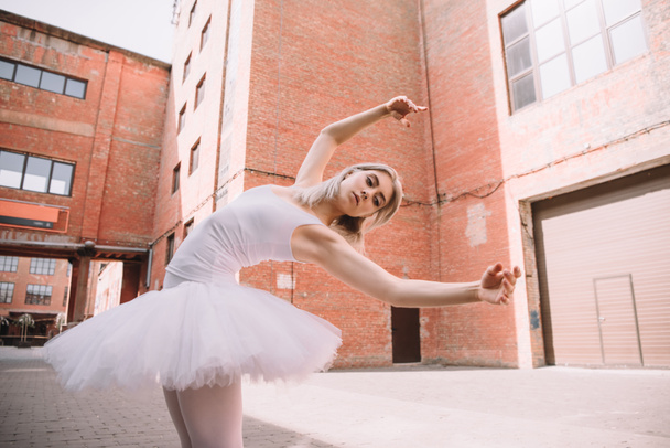 низкий угол обзора молодой балерины в белой пачке, танцующей на улице
 - Фото, изображение
