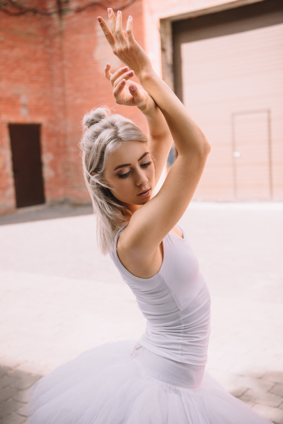 attractive young ballerina looking down while dancing on street  - Photo, Image