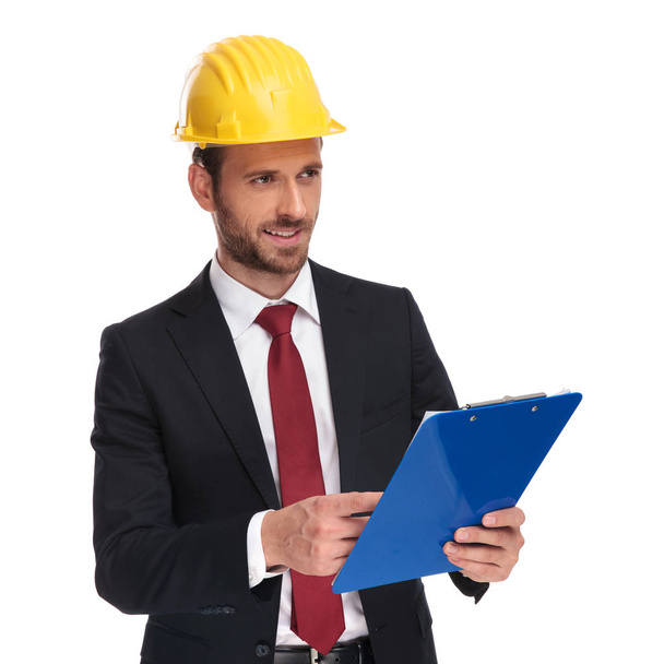 young engineer ceo holding blue clipboard looks to side while standing on white background, portrait picture - Zdjęcie, obraz