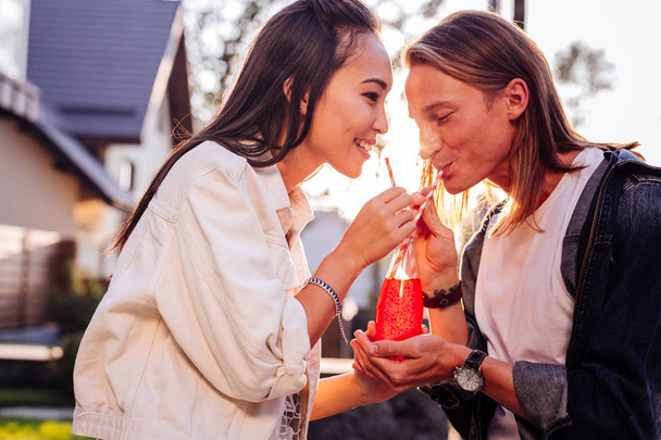 Joyful Asian woman drinking juice with her boyfriend - Фото, изображение