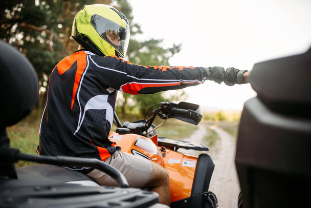 Two atv riders in helmets hits fists for good luck before extreme offroad riding, back view. Freeriding on quad bike, quadbike summer adventure - Photo, Image