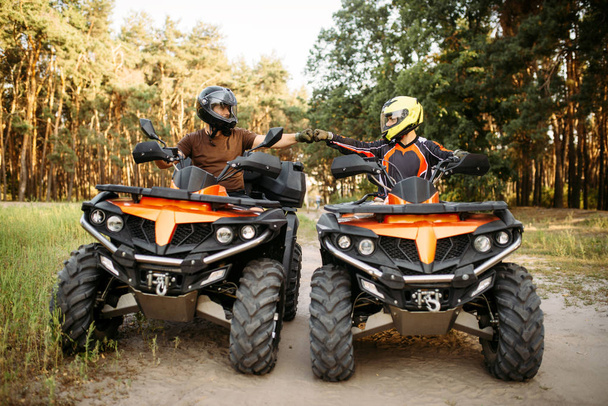 Two atv riders in helmets hits fists for good luck before dangerous extreme offroad riding, front view, summer forest on background. Freeriding on quad bike, quadbike adventure - Photo, Image