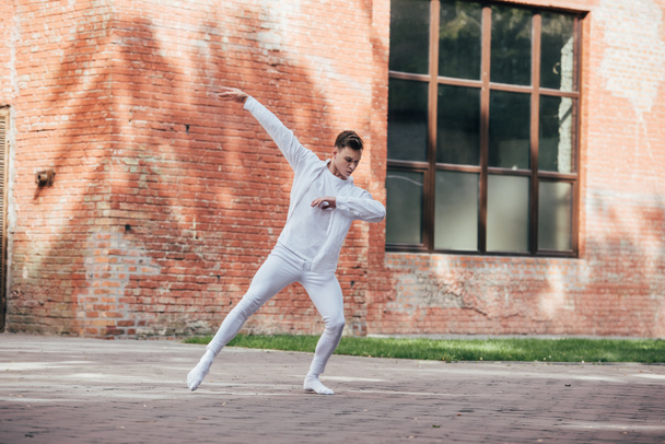 handsome young man in white clothes dancing on urban city street     - Фото, зображення
