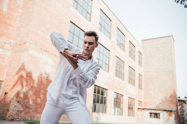 low angle view of handsome young man in white clothes dancing on street  - Foto, Imagem