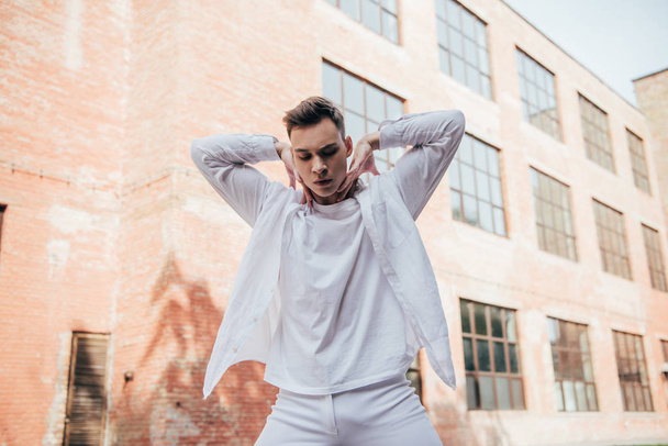 low angle view of handsome young man in white clothes dancing on urban street      - Photo, Image