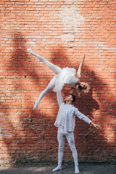 νεαρό ζευγάρι χορευτές εκτελούν χορό μπαλέτου κοντά σε τοίχο από τούβλα  - Φωτογραφία, εικόνα