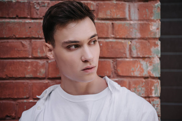 portrait of handsome young man looking away near brick wall  - Fotografie, Obrázek