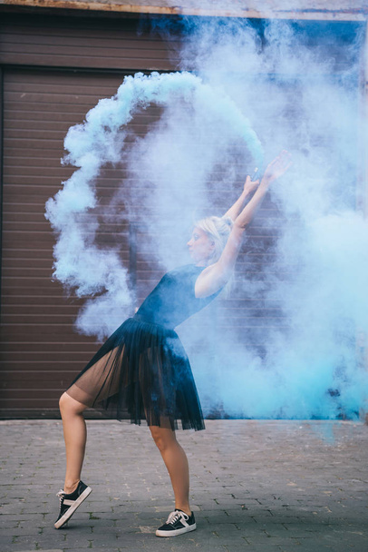 通りに青い煙で踊る若い女性の側面図   - 写真・画像