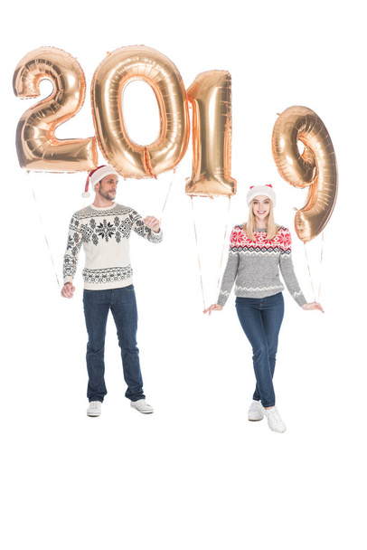 stylish couple in sweaters and santa claus hats with 2019 balloons isolated on white, 2019 new year concept - Photo, Image
