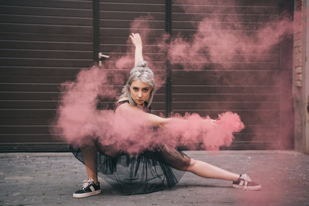 krásná dívka tančí v růžové kouře a při pohledu na fotoaparát na ulici  - Fotografie, Obrázek