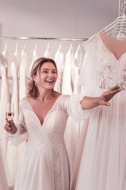 Amazing dress. Joyful happy woman stretching out her hand while wanting to touch a beautiful wedding dress - Foto, Bild