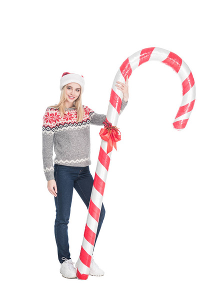 young woman in sweater and santa claus hat holding toy candy isolated on white - Foto, Imagen