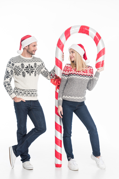 young couple in santa claus hats and sweaters with toy candy isolated on white - Foto, imagen