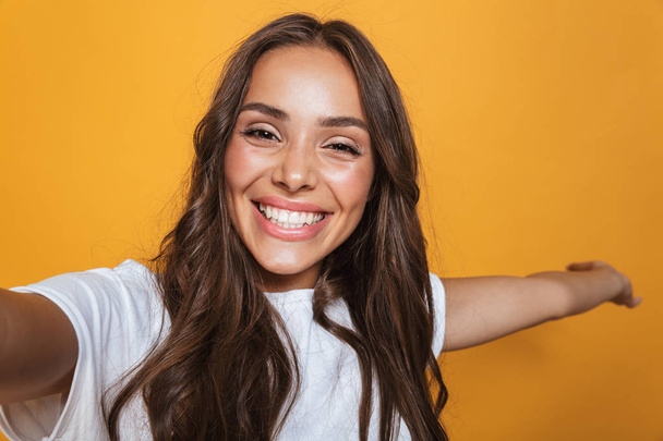 Retrato de mulher caucasiana 20s com cabelos longos rindo ao tirar foto selfie isolado sobre fundo amarelo
 - Foto, Imagem