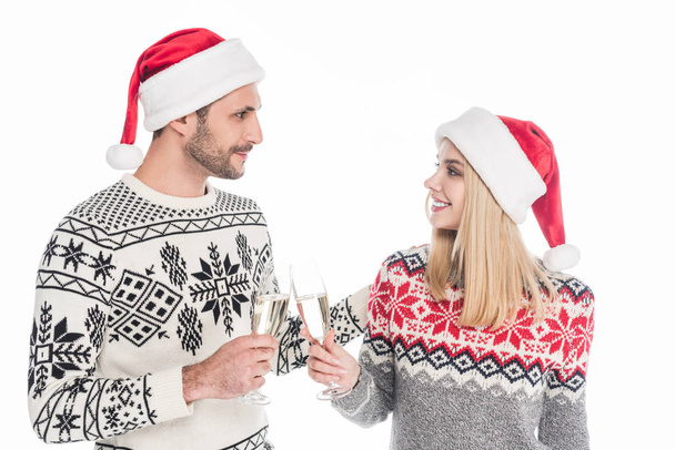 couple in sweaters and santa claus hats clinking glasses of champagne isolated on white - Fotó, kép