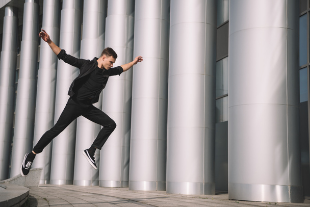young male contemporary dancer in black clothes jumping on street    - 写真・画像