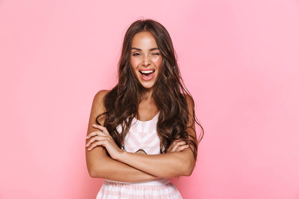 Image of cute woman 20s with long hair wearing dress smiling at camera with arms crossed isolated over pink background - Fotografie, Obrázek