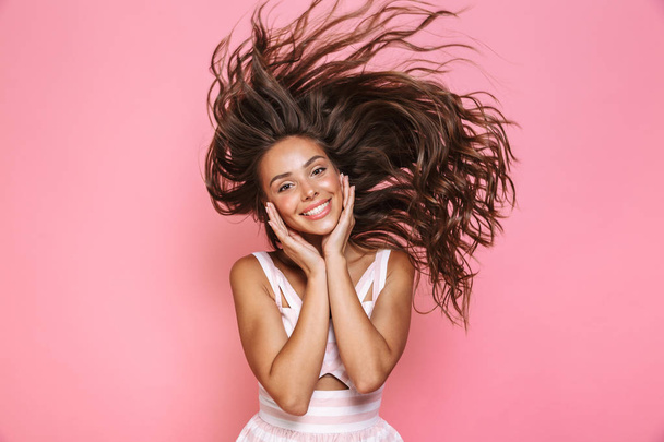 Photo of cheerful woman 20s wearing dress laughing and shaking her long brown hair isolated over pink background - Fotoğraf, Görsel