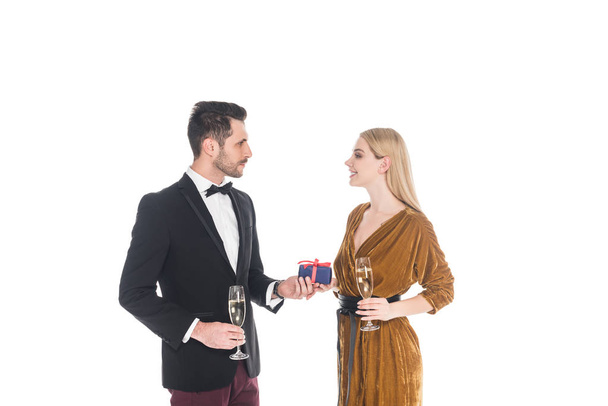 elegante hombre presentando regalo a la novia sonriente con copa de champán aislado en blanco
 - Foto, Imagen